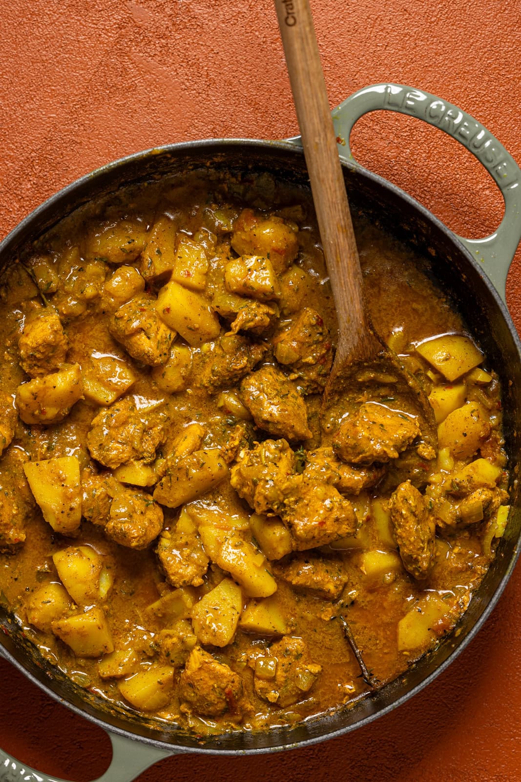 Curry chicken in a grey pot with a wooden spoon.
