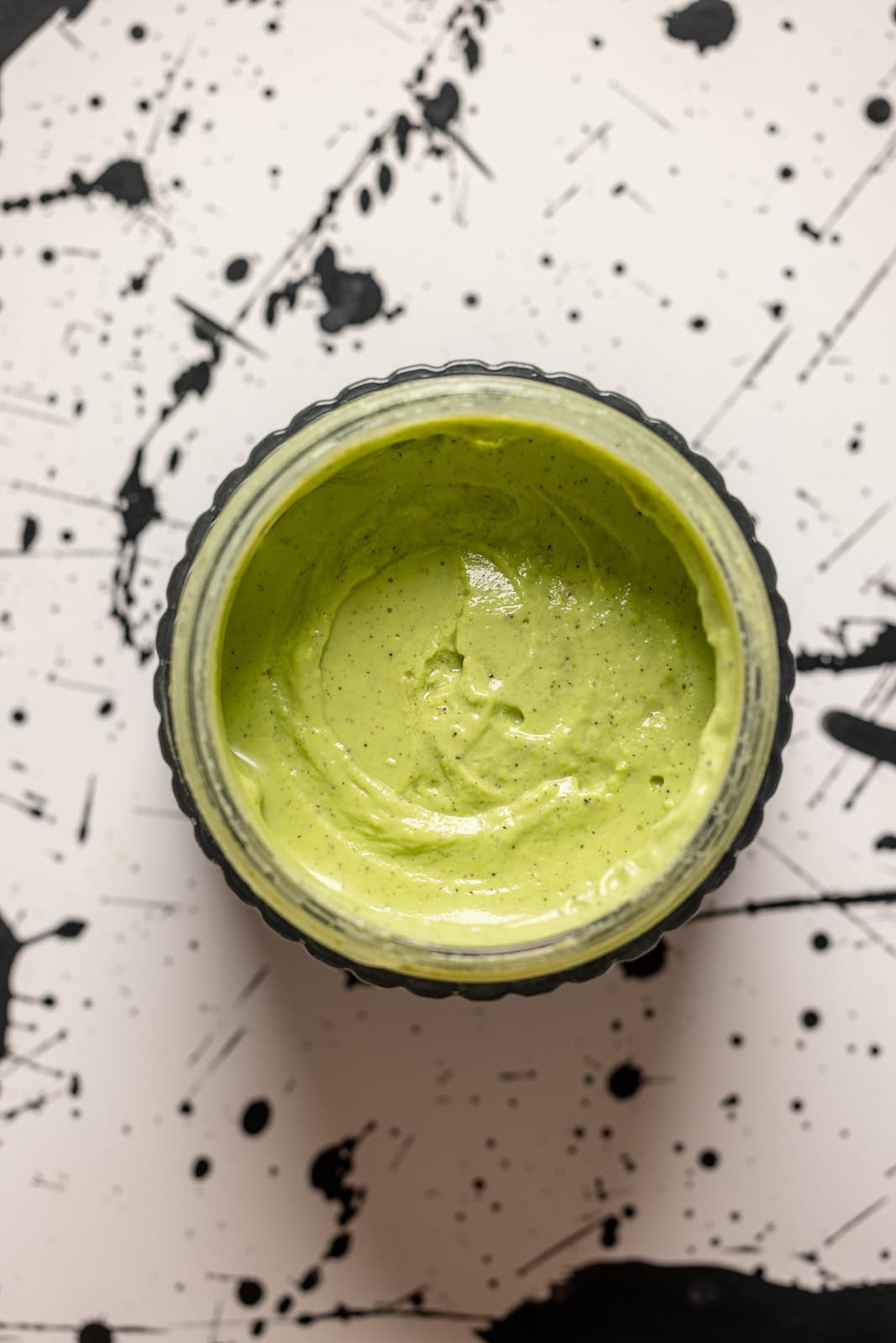 Green goddess sauce on a white table with black spots.