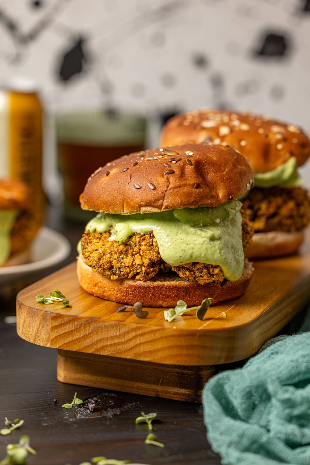 Two crispy chicken sandwiches on a wooden platter with drinks in background. 