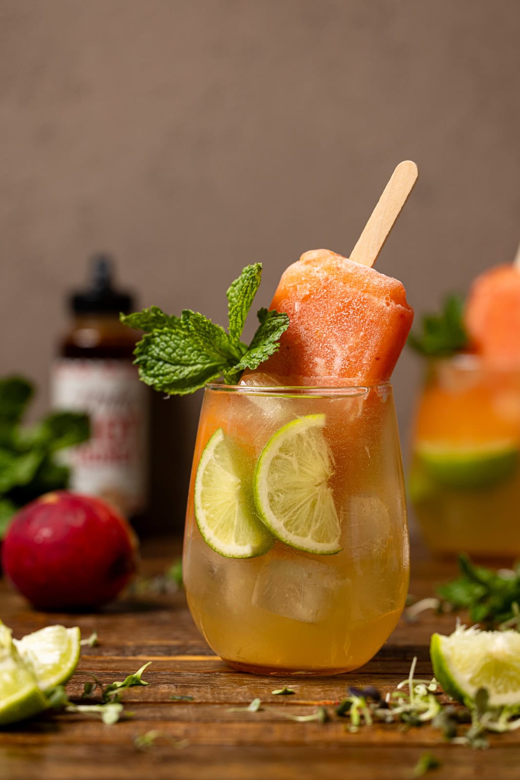 Two glasses of peach hot honey mocktails with lime and popsicles. 
