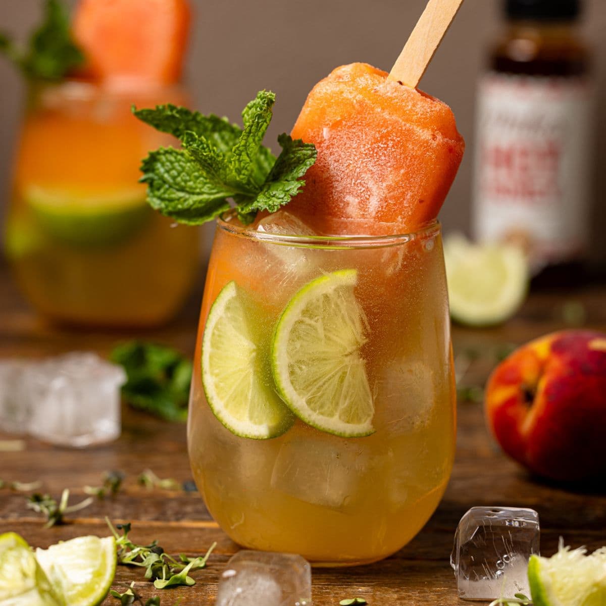 Overview of mocktails in two glasses with lime, a peach, ice cubes, and hot honey.