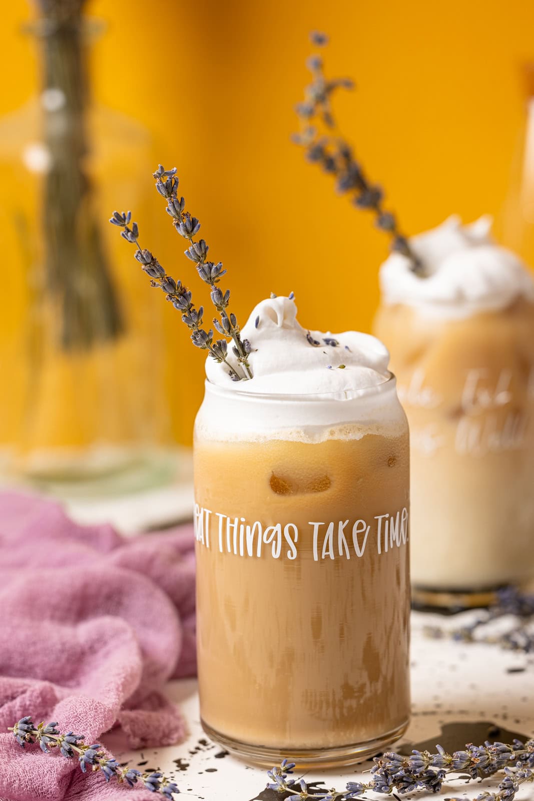 Up close shot of iced lattes with a yellow background and lavender flowers. 