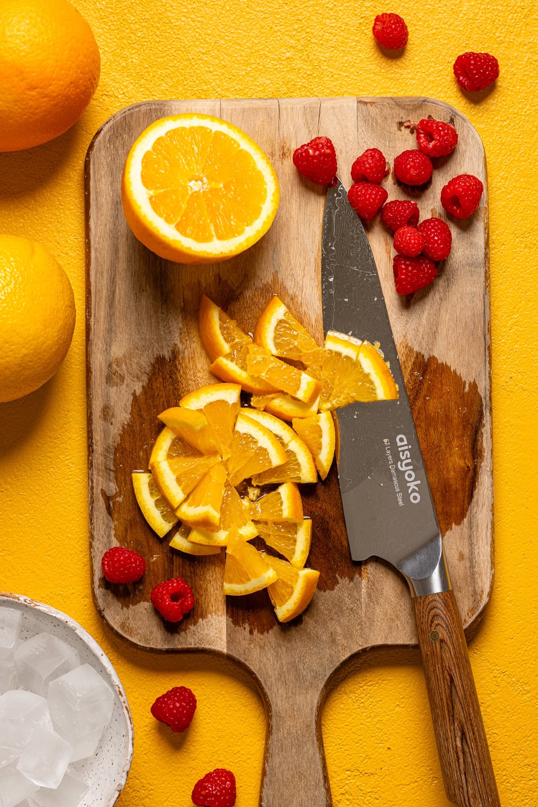 Diced oranges and raspberries on a cutting board with a knife.