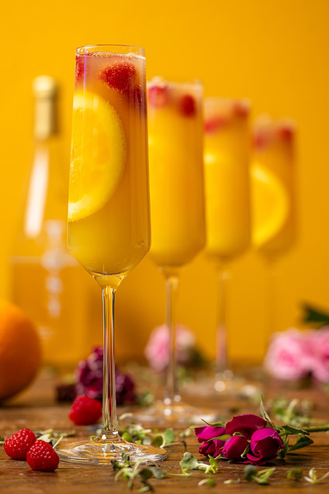 Four glasses of mimosas with flowers and raspberries.