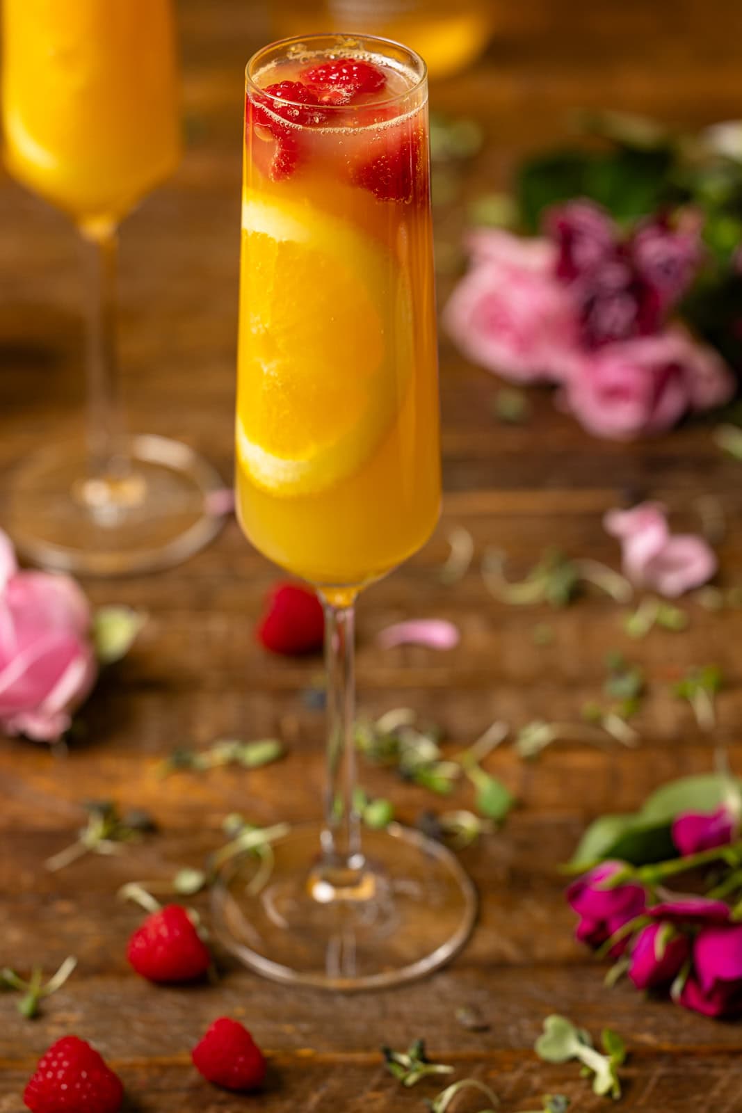 Overview of mimosas on a brown wood table with flowers and raspberries. 