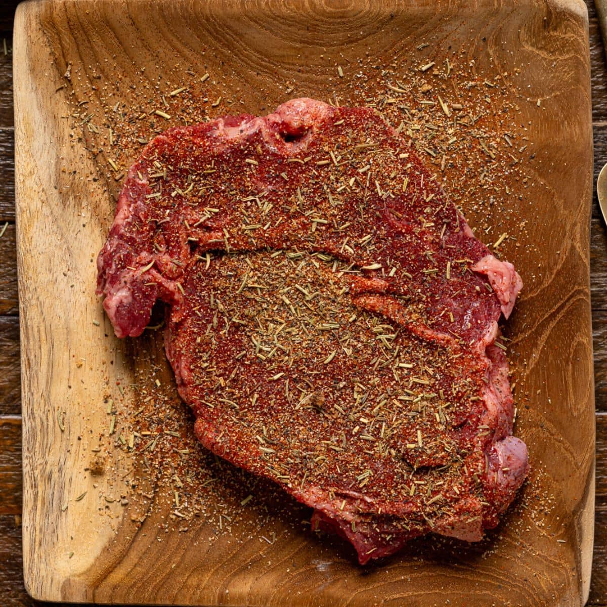 Seasoned steak on a brown wood plate.