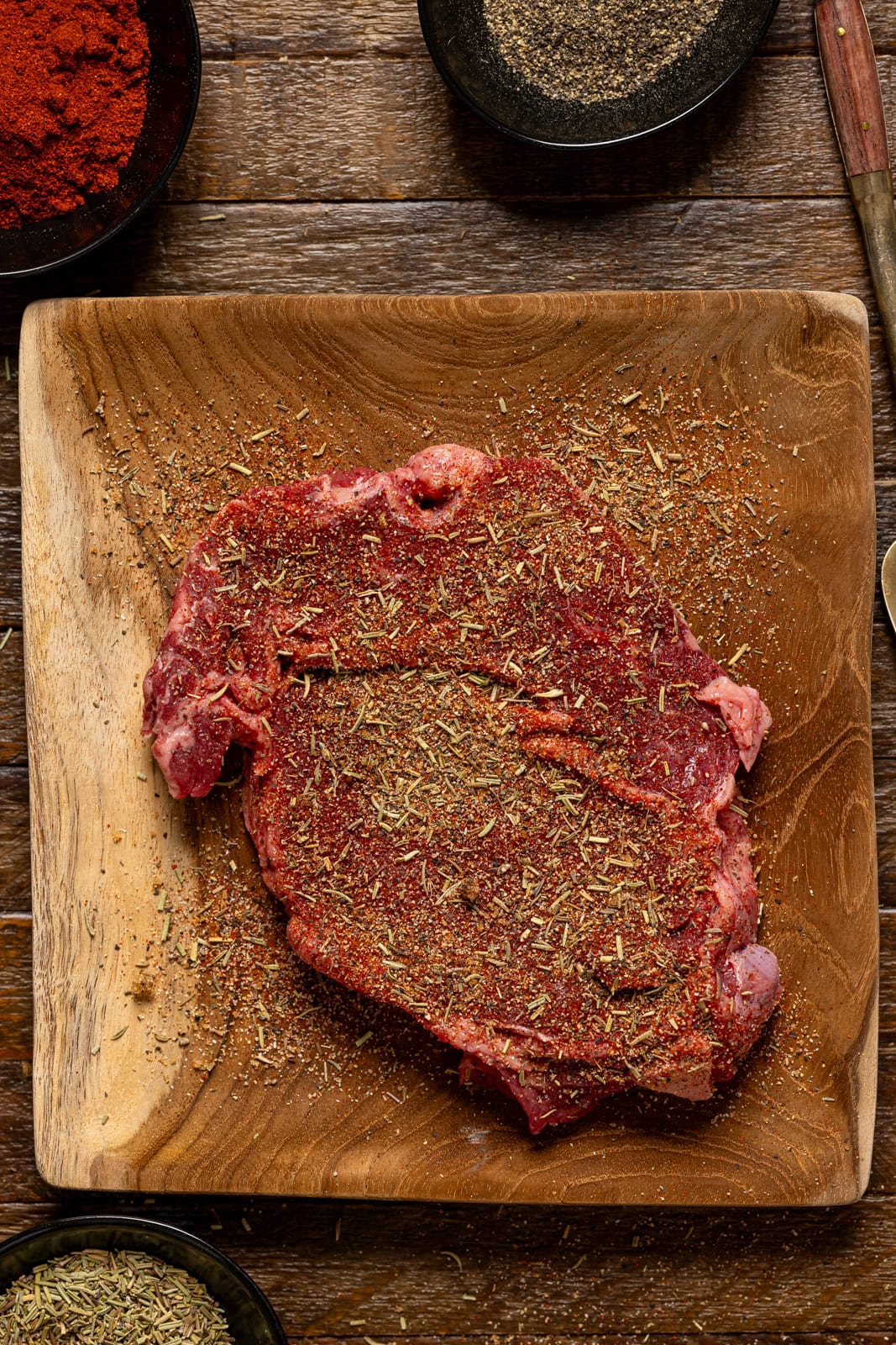 Seasoned steak on a brown wood plate.
