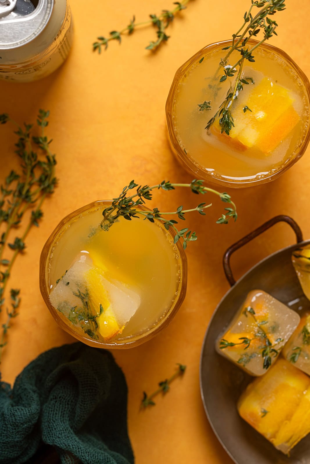 Overhead shot of drinks and ice cubes on an orange table.