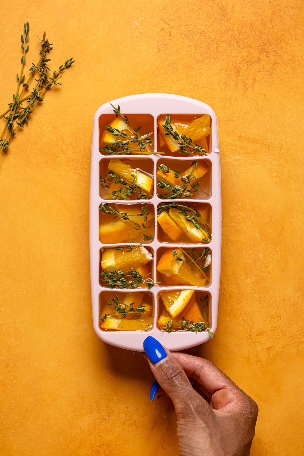 Ice tray being held on an orange table with ingredients. 