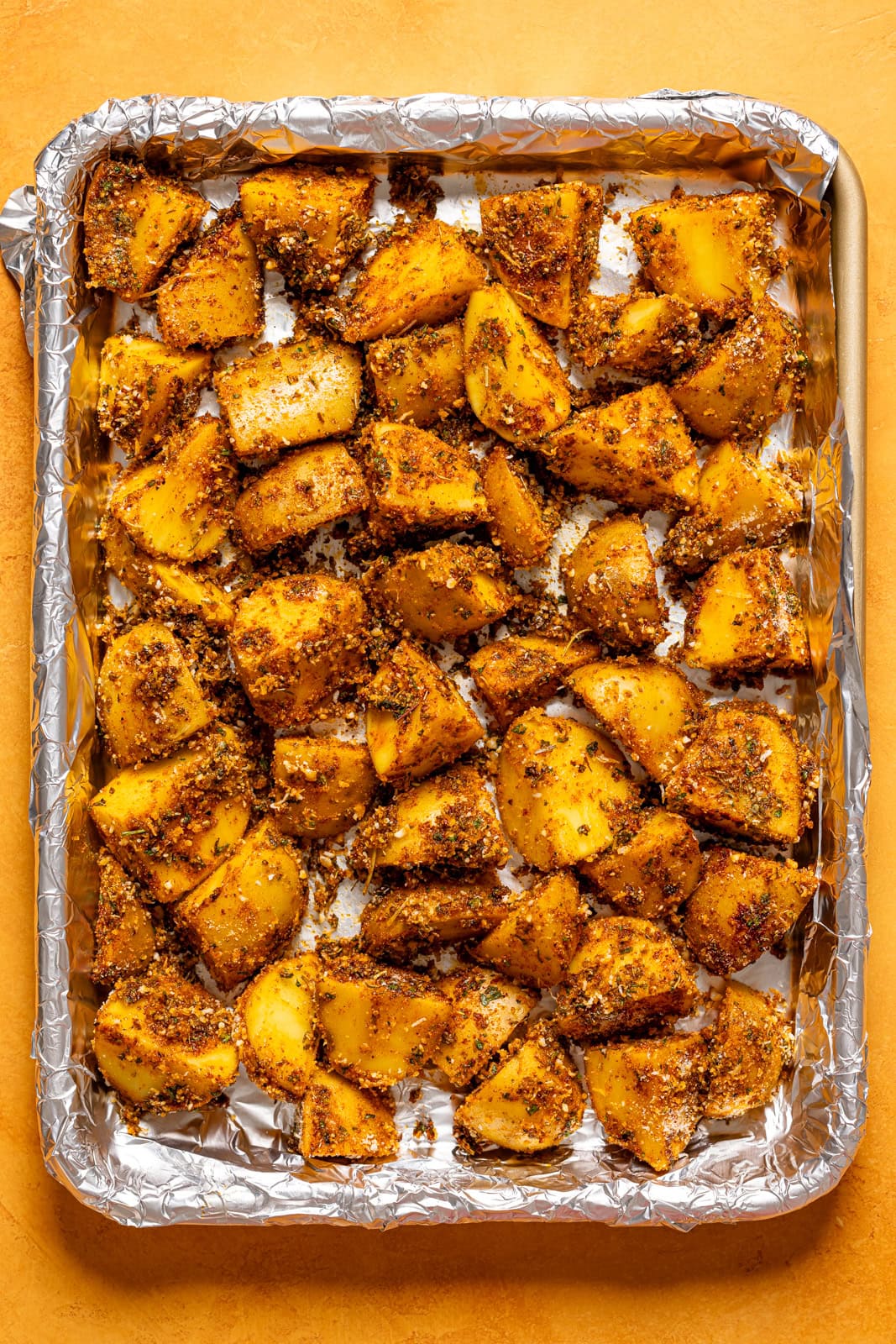 Coated potatoes on a baking sheet lined with foil.