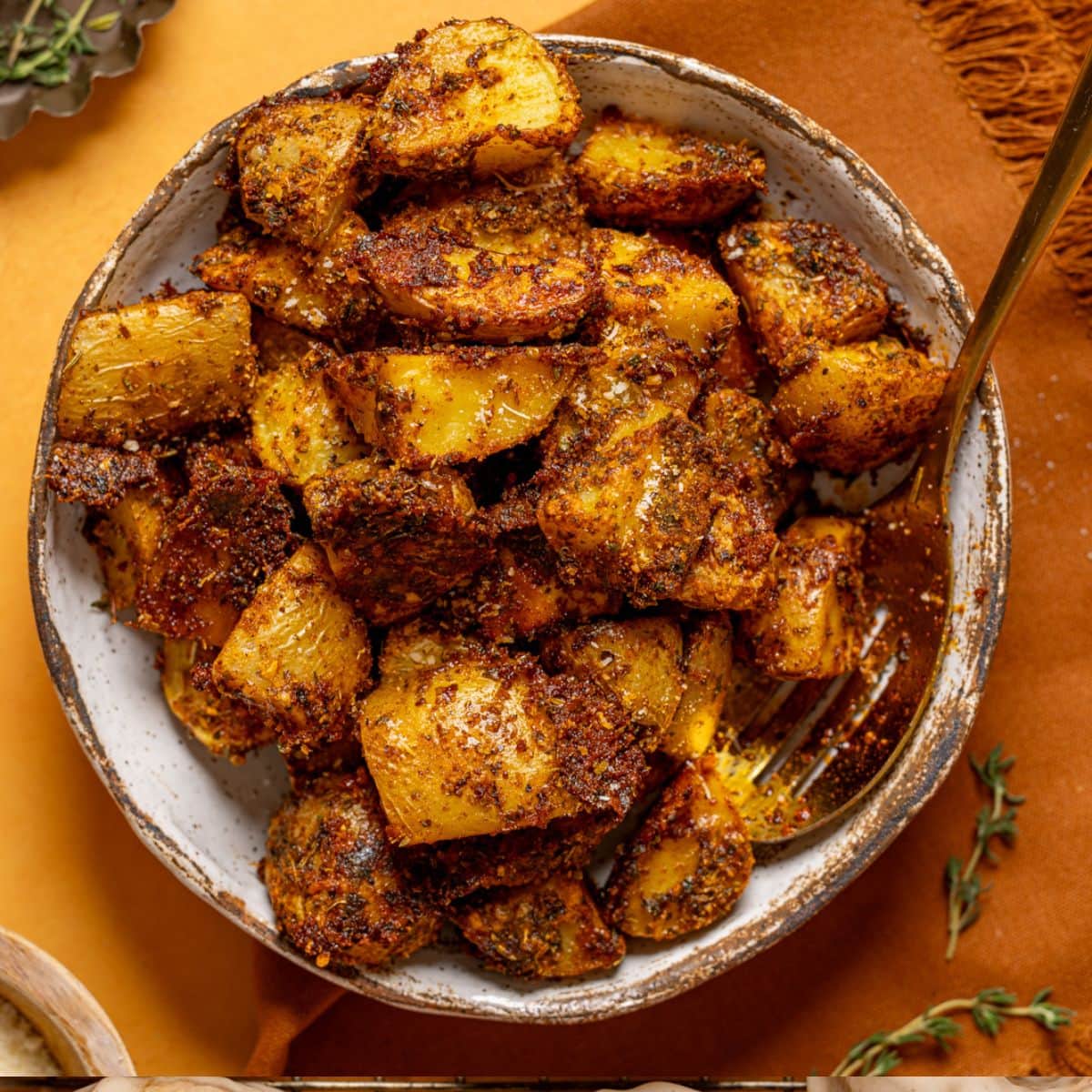 Roasted potatoes in a dish with a spoon and parmesan.