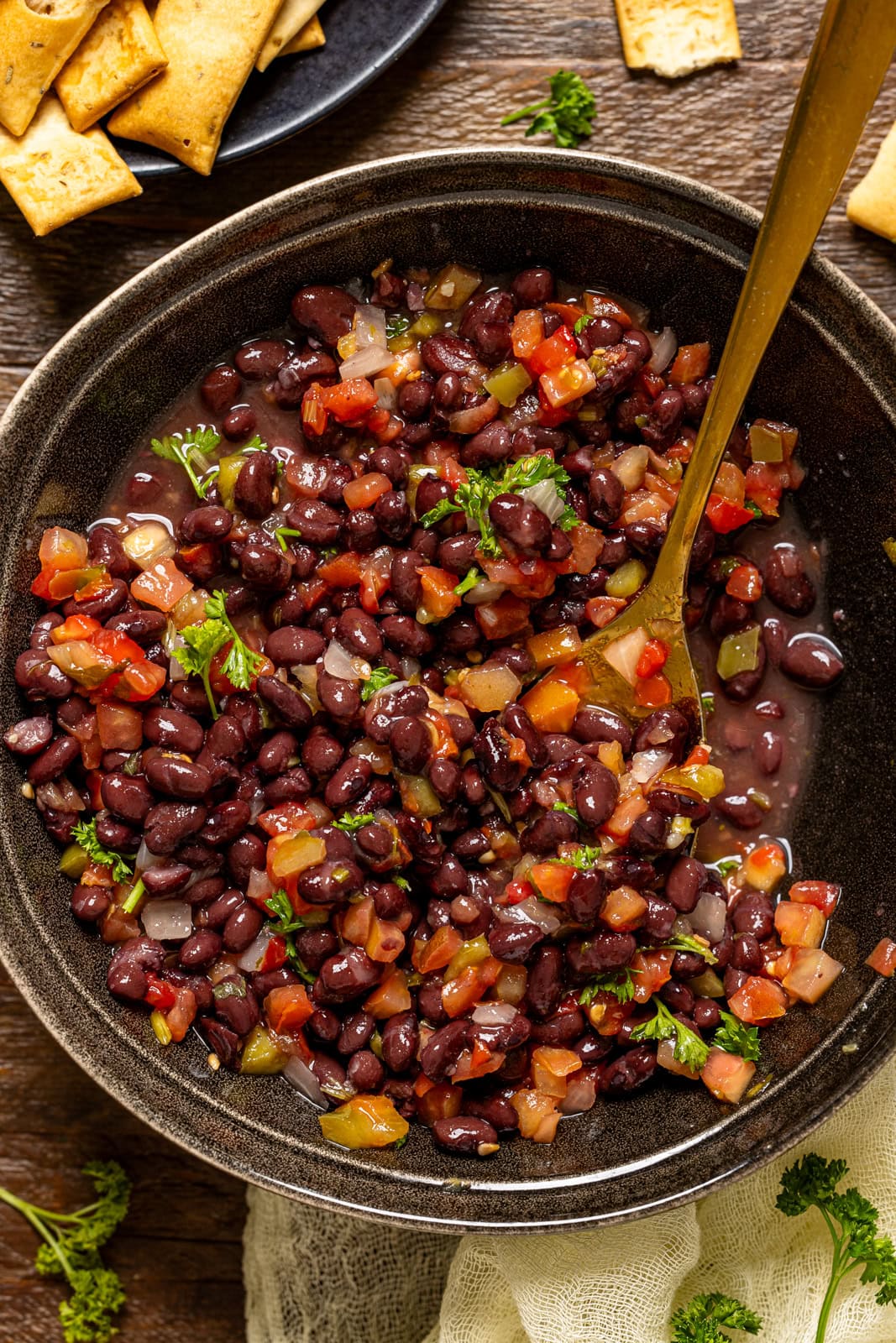Up close shot of black bean salad in a black bowl with a gold spoon.