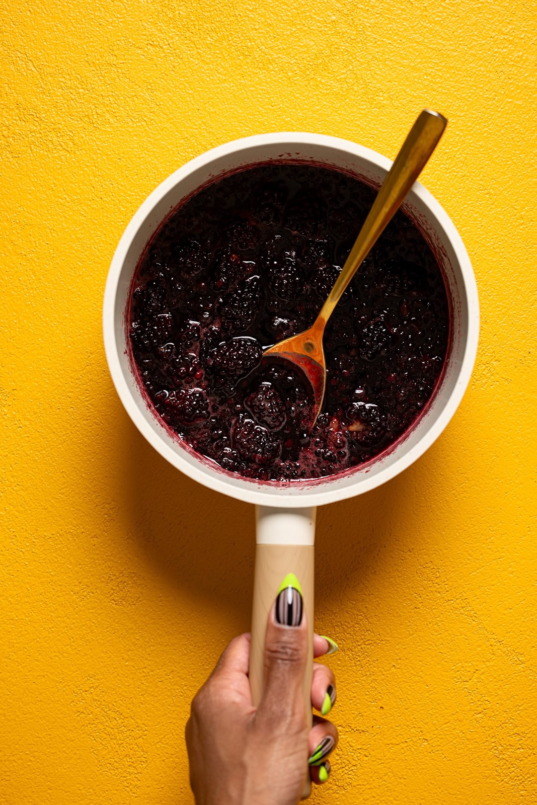 Blackberry sauce in a pot being held with a spoon.