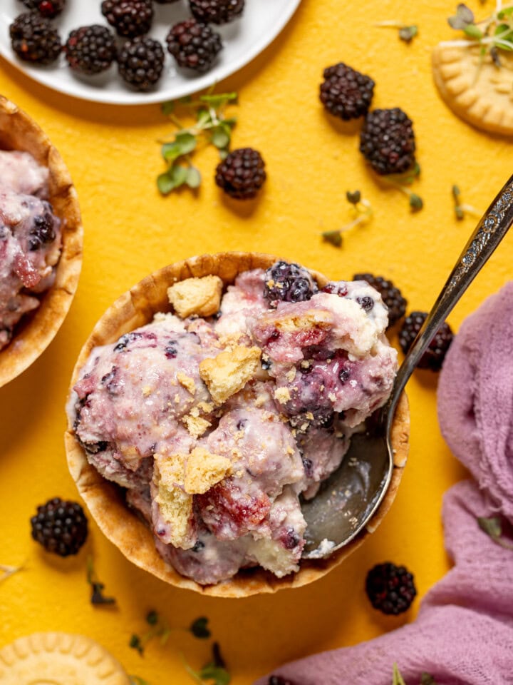 Ice cream in two cones with a spoon, blackberries, and cookies.