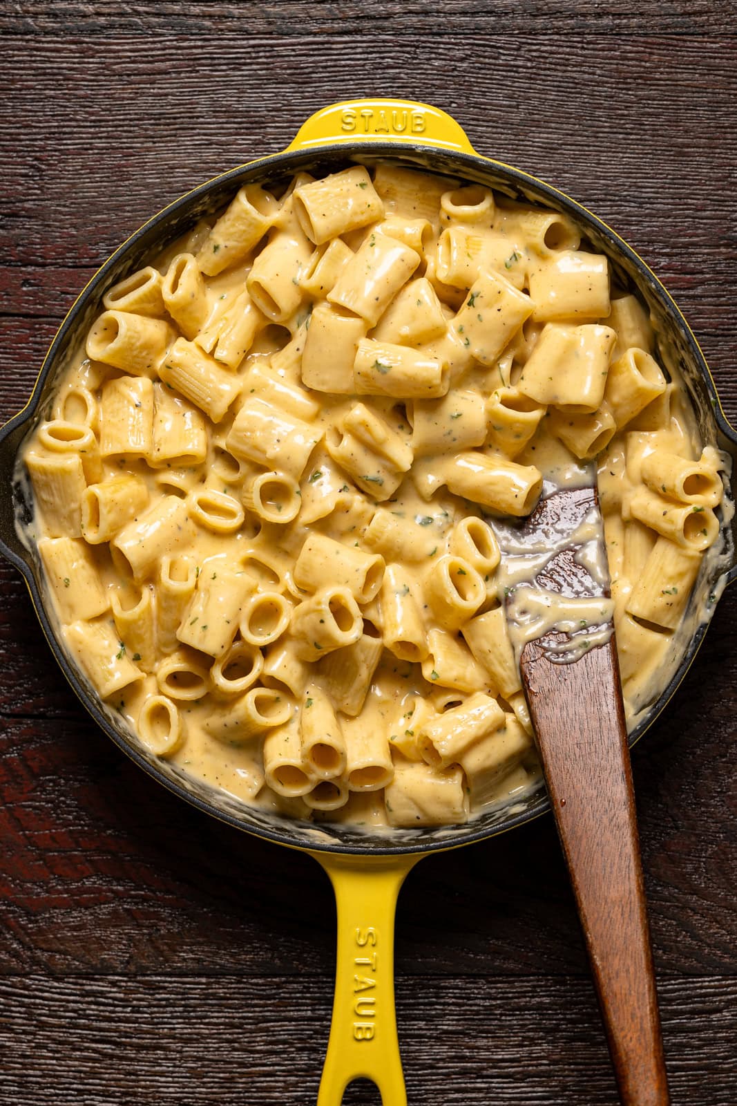 Mac and cheese in a yellow skillet with a wooden spoon.