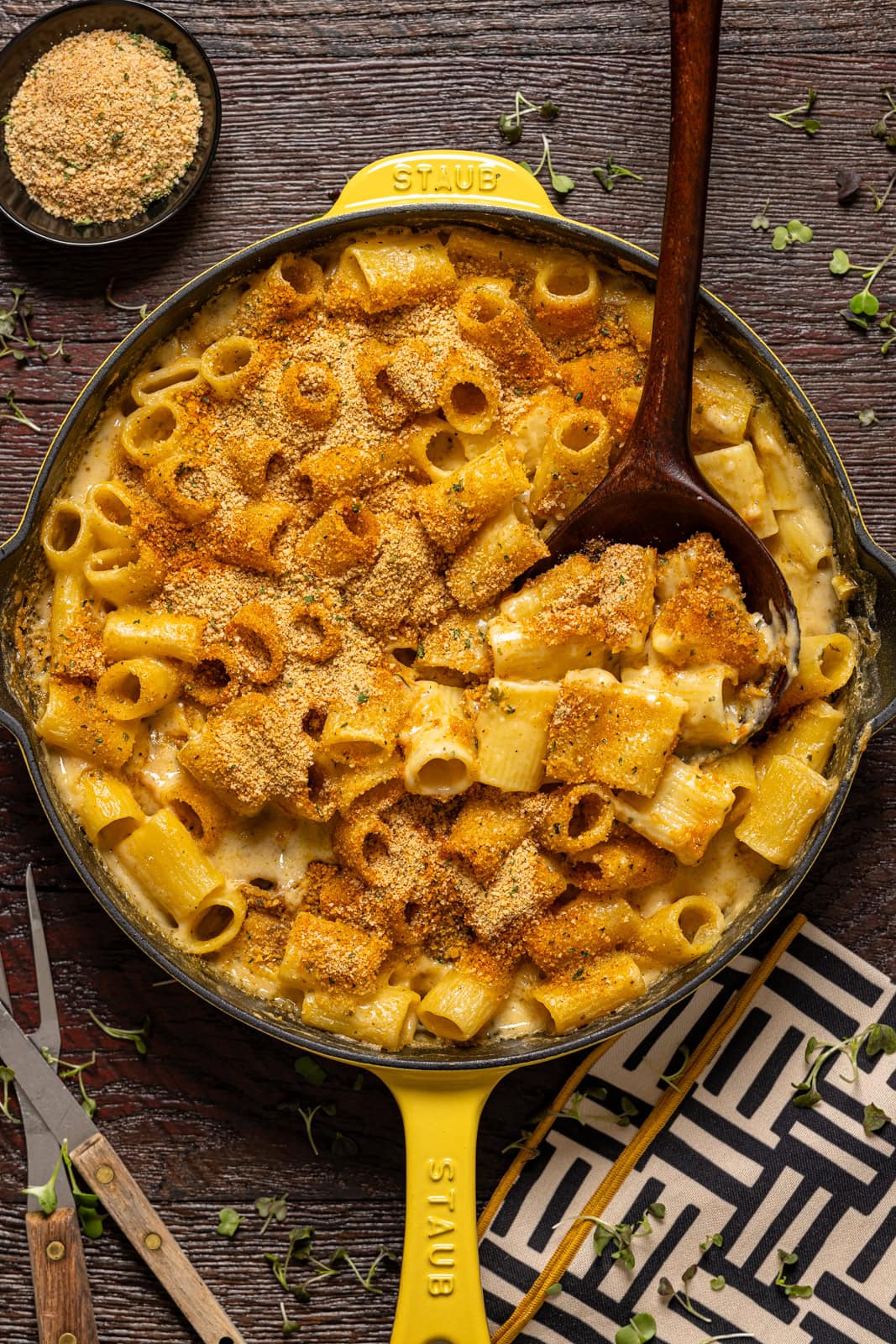 Baked mac and cheese in a yellow skillet with a wooden spoon and forks.