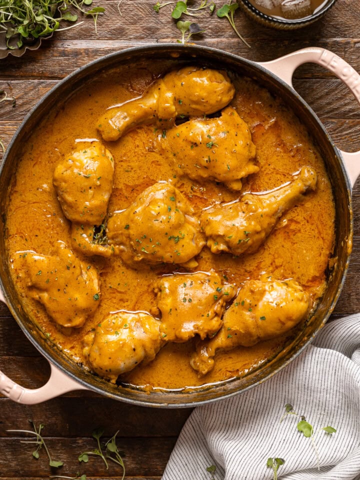 Chicken in a white pot on a brown wood table with a side of drink.