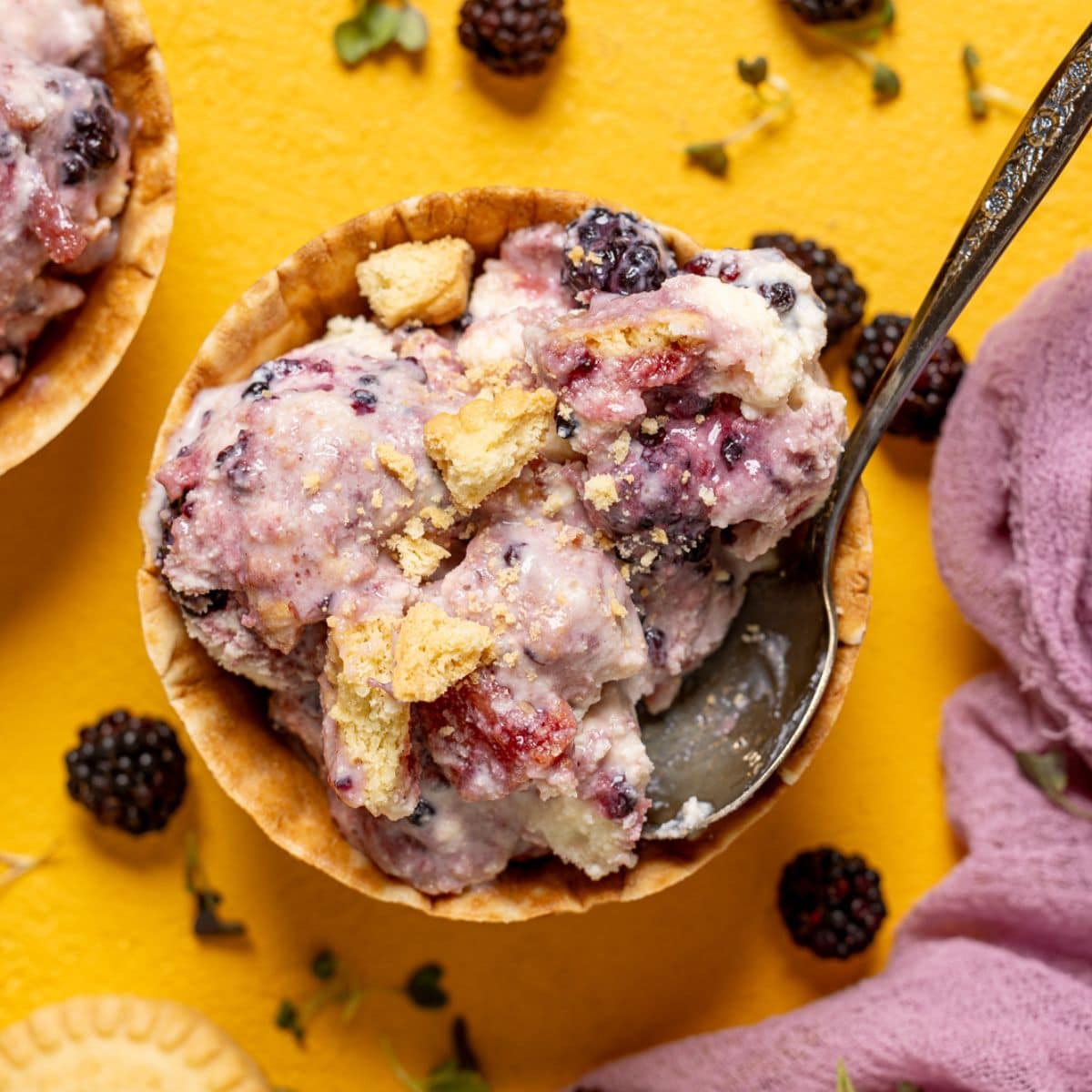 Ice cream in two cones with a spoon, blackberries, and cookies.
