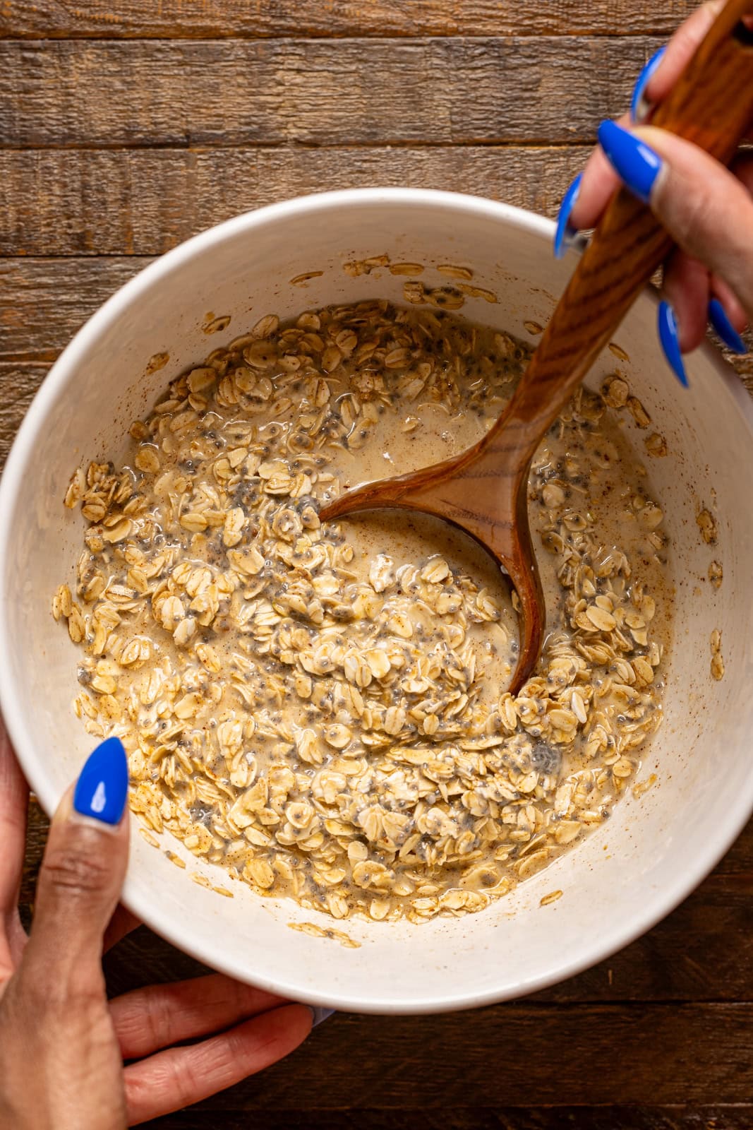 Oatmeal ingredients being stirred in a bowl with a wooden spoon.