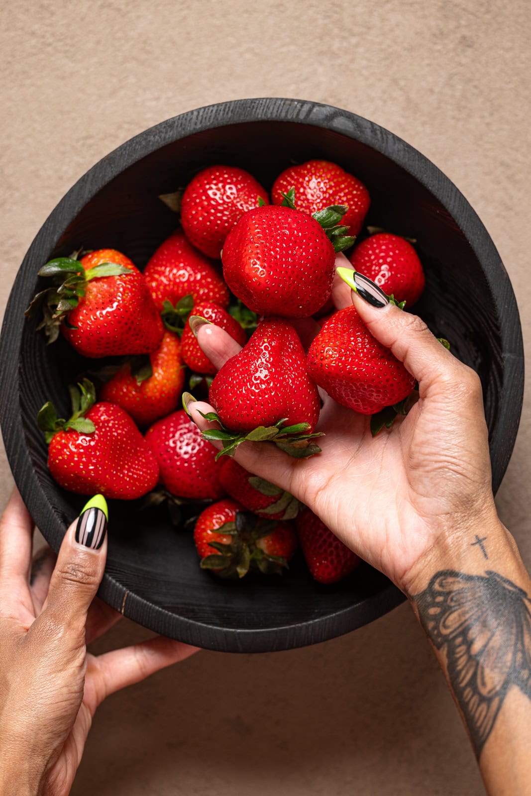 Fresh strawberries being held in a black wood bowl.