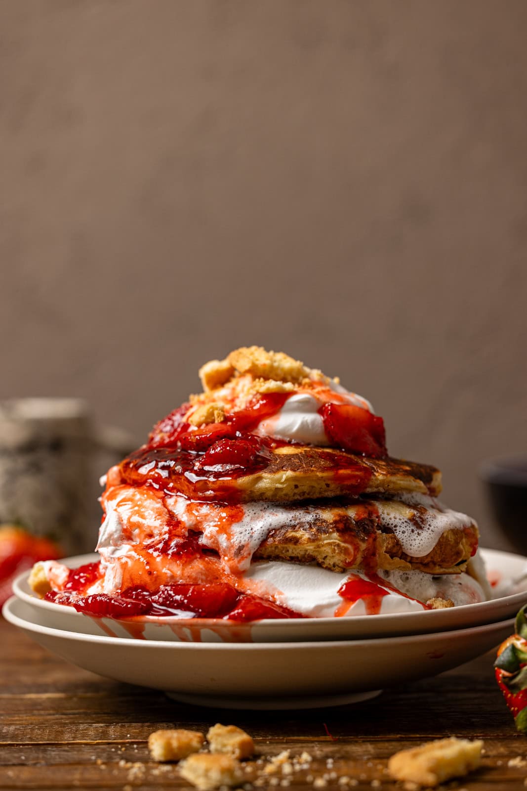 Stack of pancakes with whipped cream and strawberries on white plates.