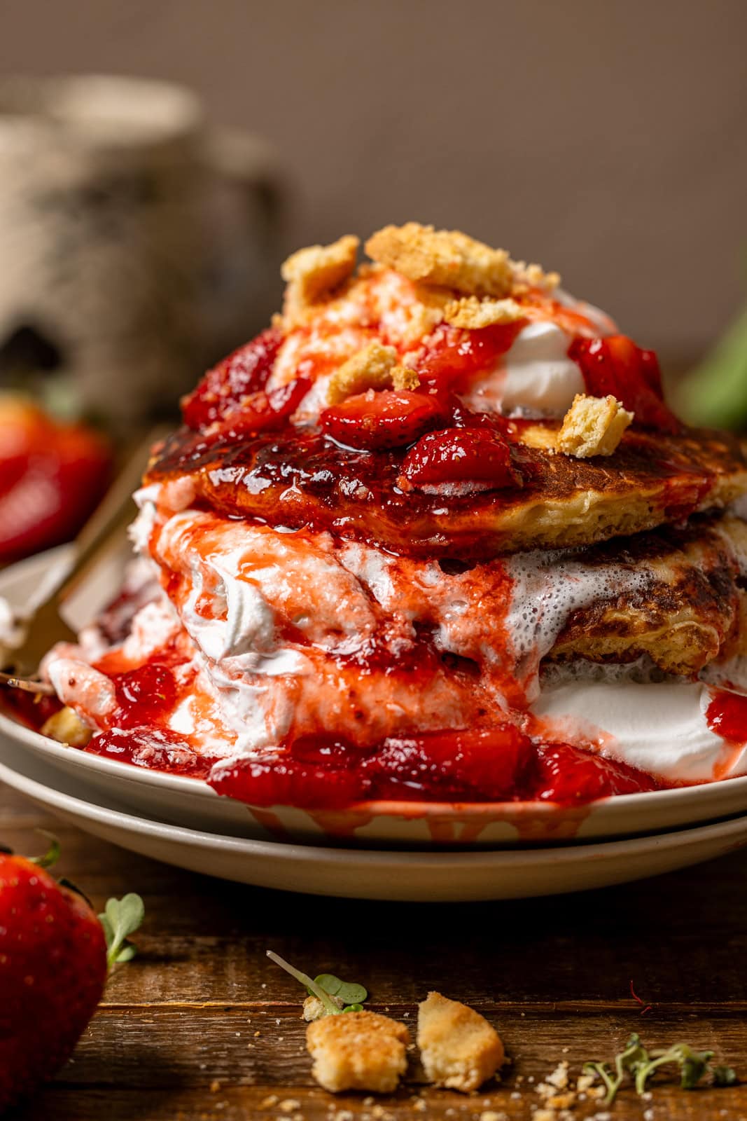 Up close shot of stack of pancakes with whipped cream and strawberries.