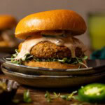 Up close shot of veggie burger on two plates with a drink in background.