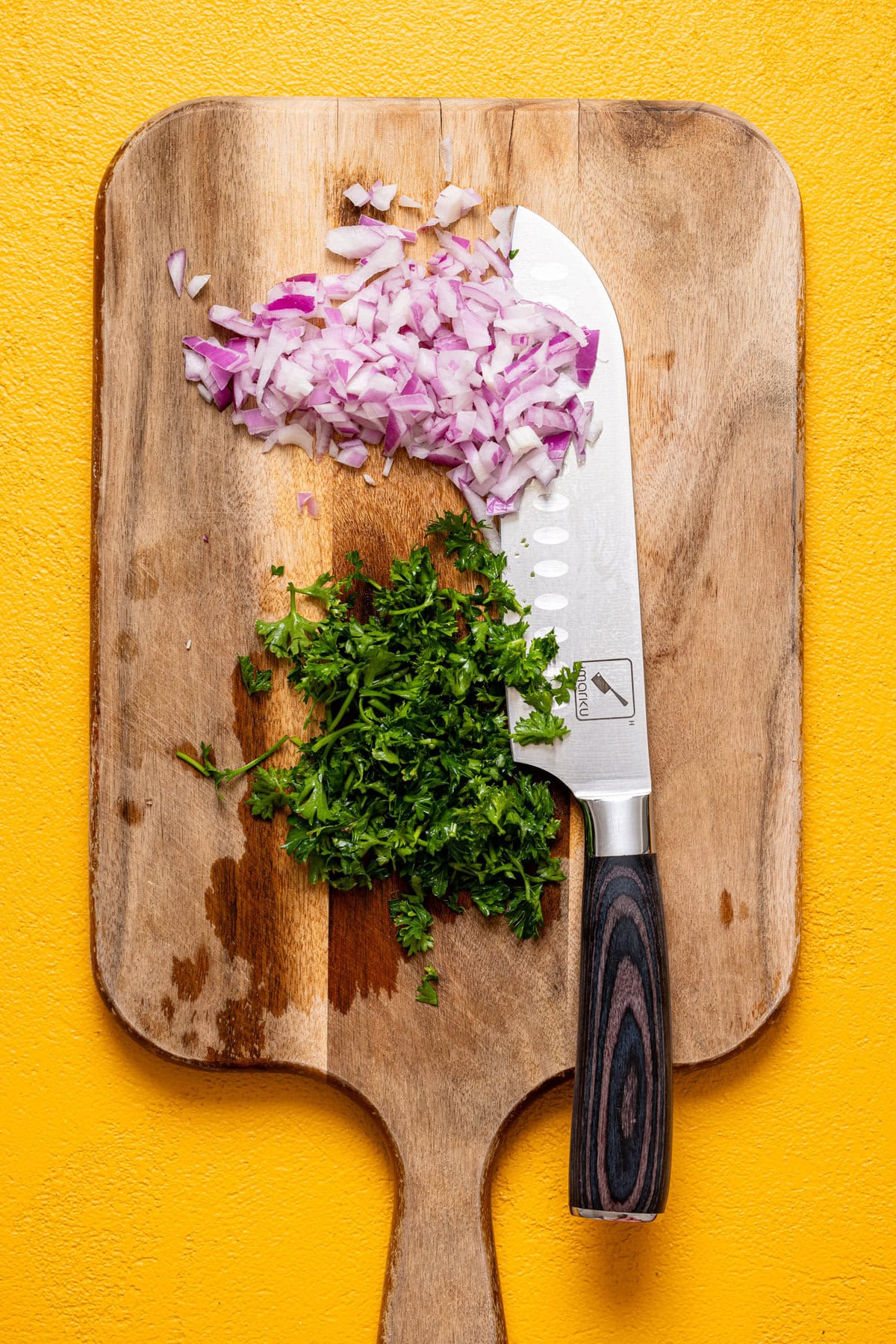 Chopped herbs on a cutting board with a knife.