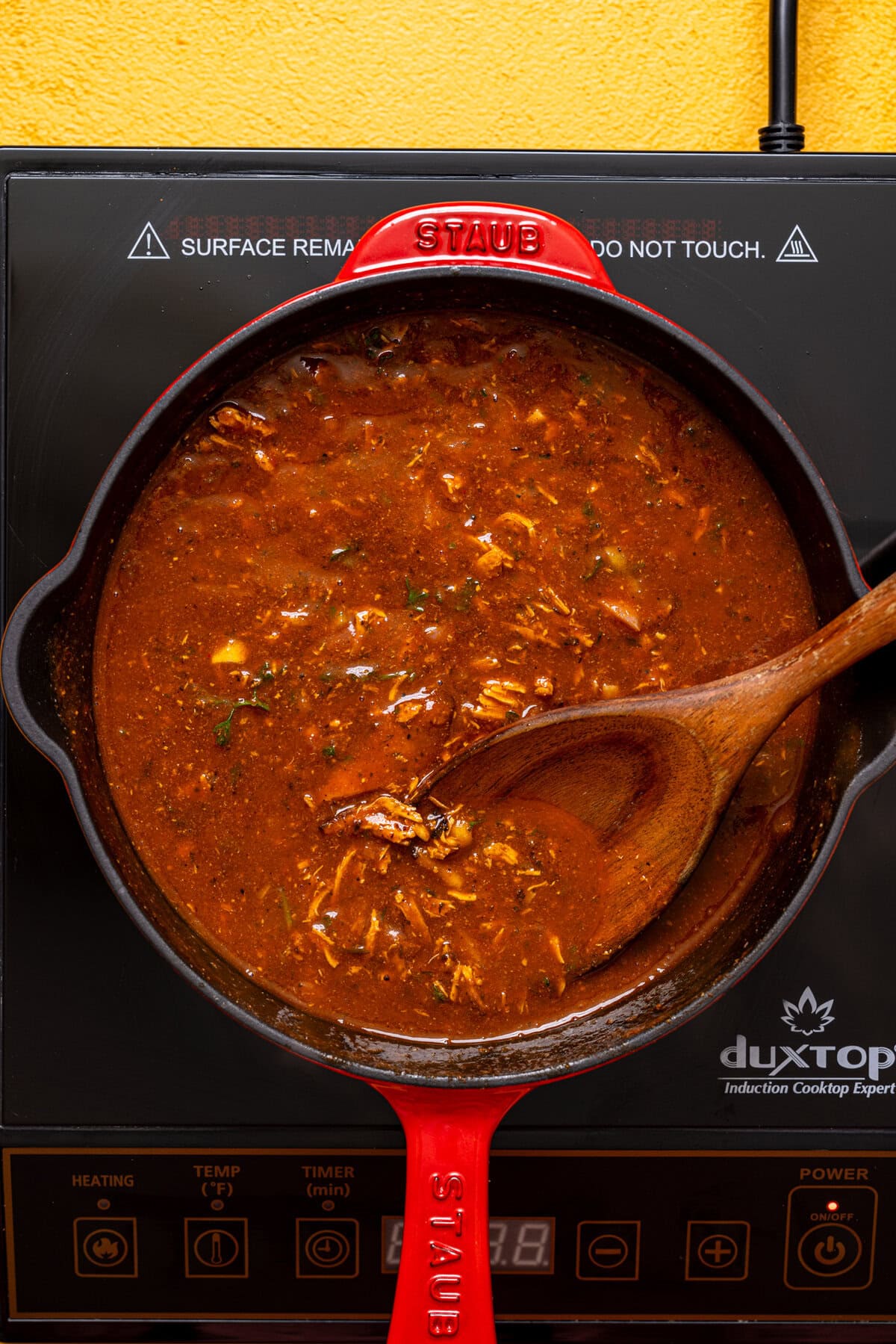 Shredded chicken in birria sauce in a skillet over the stovetop. 