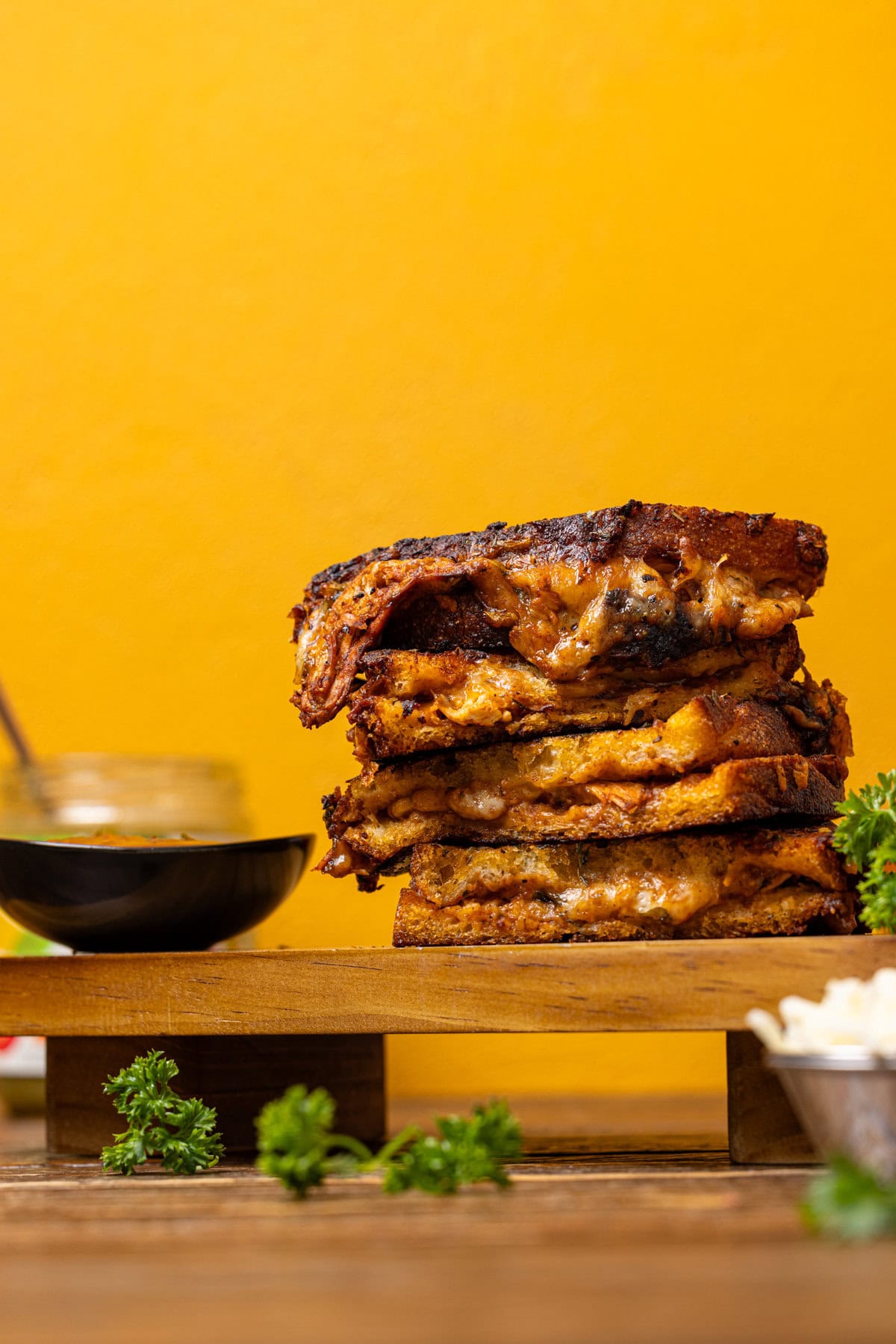 Stack of grilled cheese on a wooden platter with sauce. 