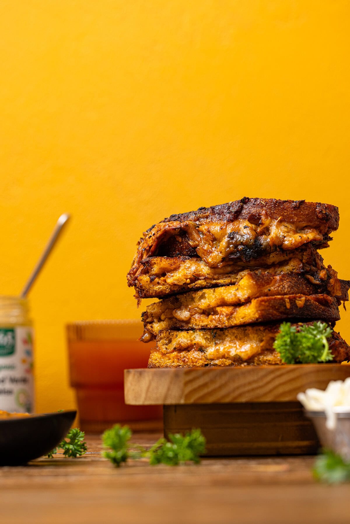 Stack of Birria grilled cheese with a drink and sauce in the background. 