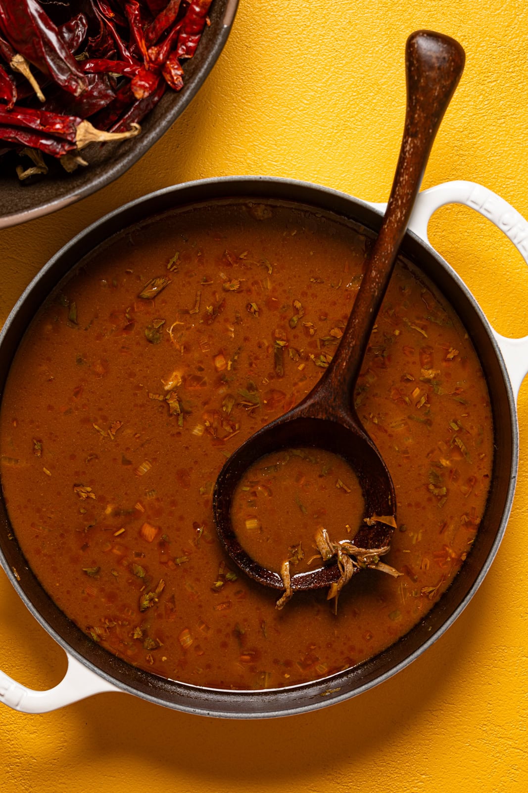 A white pot full of Birria sauce with a wooden spoon.