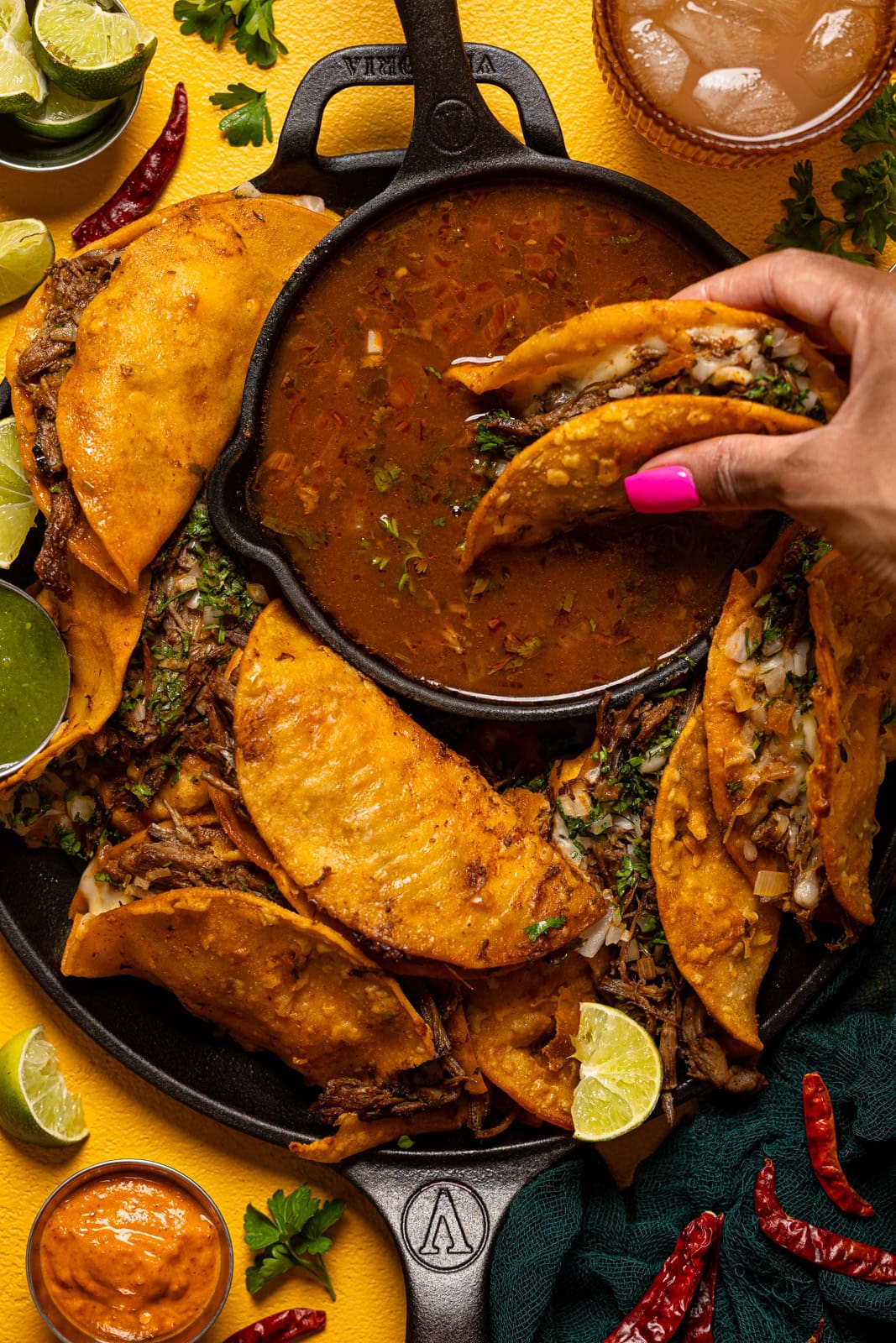 Birria tacos being held and dipped in consomme sauce.