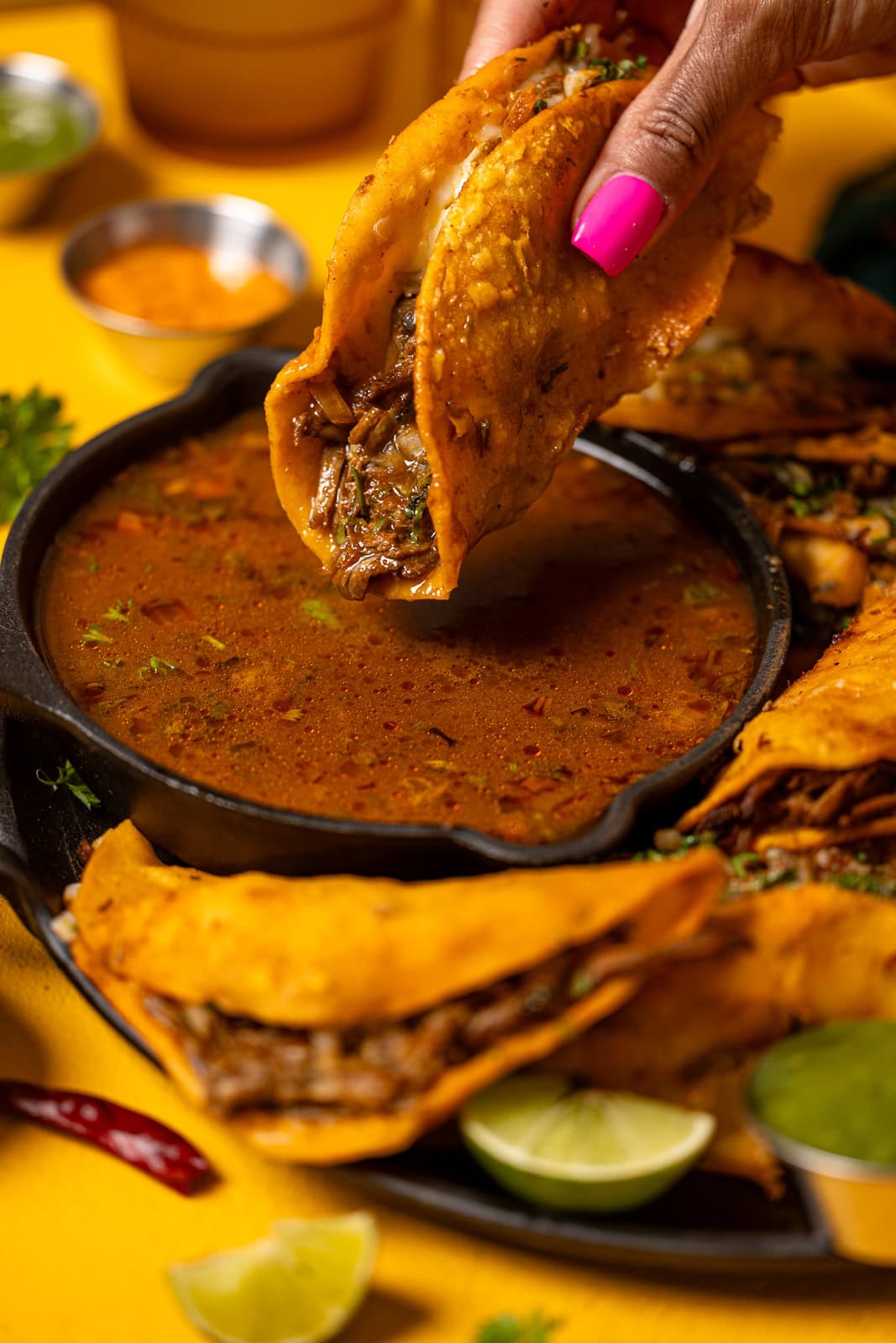 Taco being held in hand and dipped in sauce.