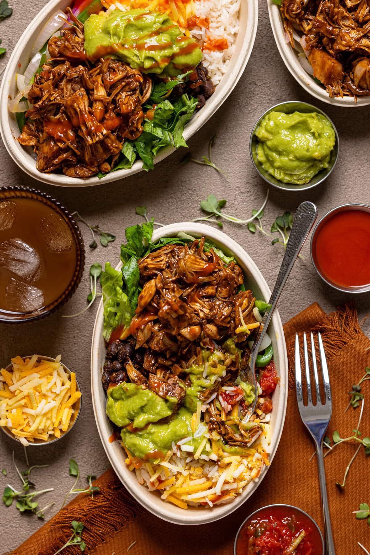 Overview shot of two burrito bowls with drinks and condiments.