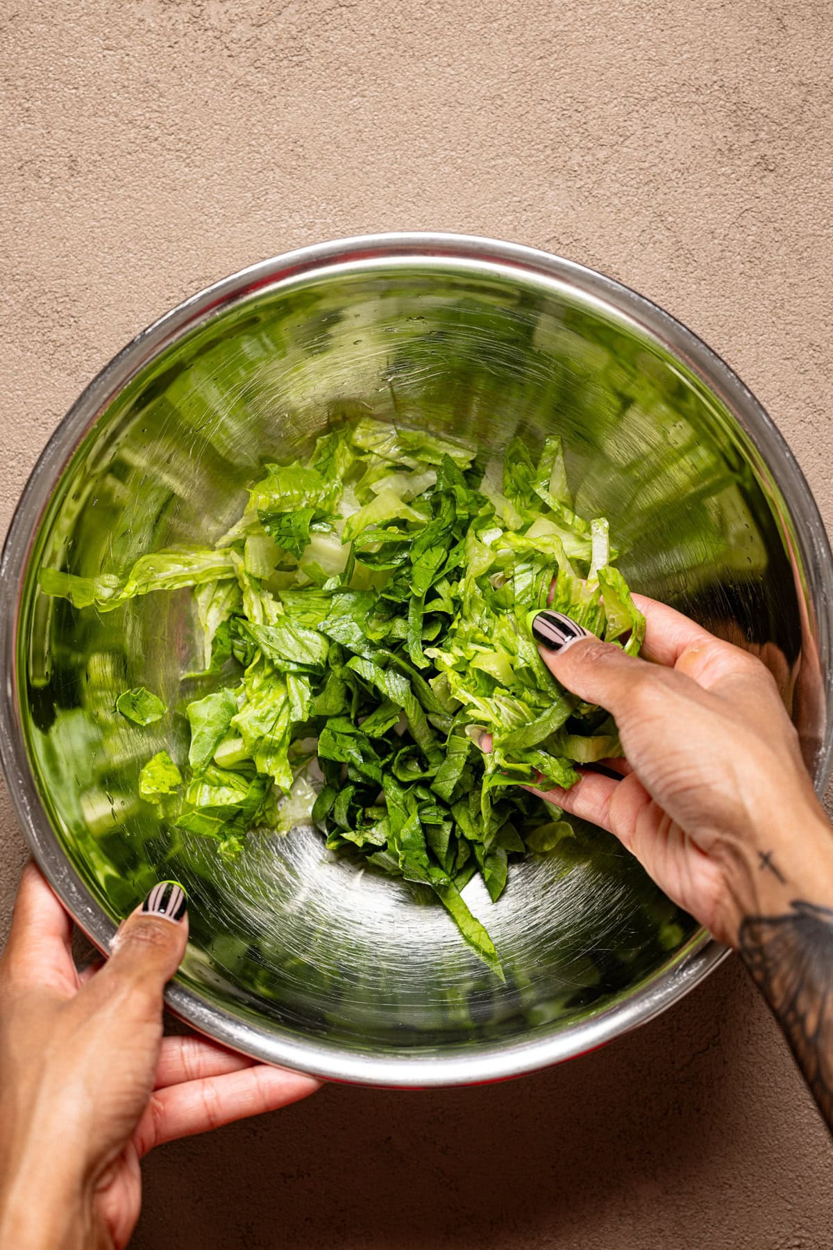 Shredded lettuce in a metal bowl being held.