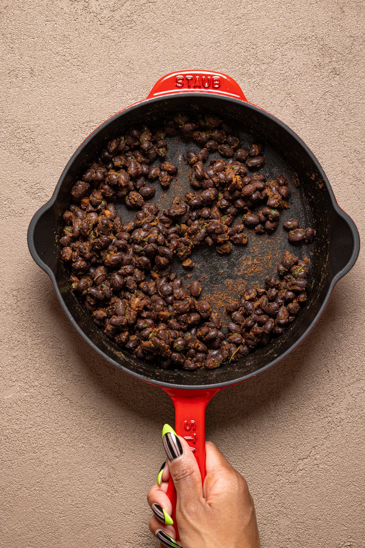 Cooked black beans being held in a red skillet. 