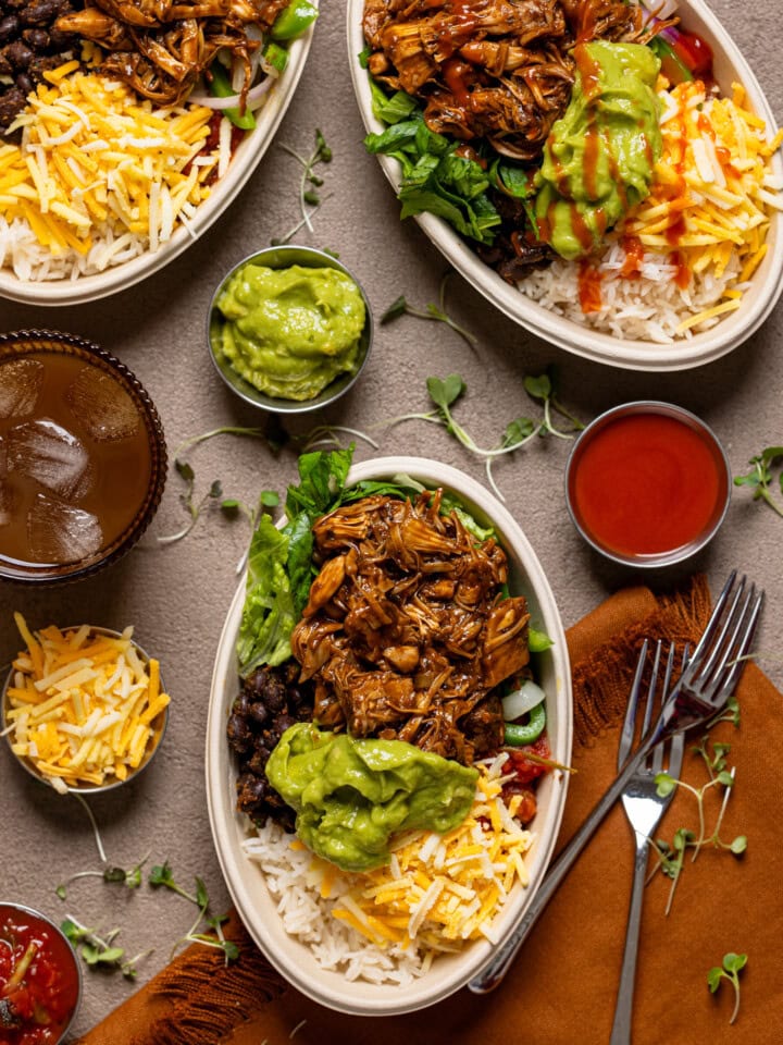Three burrito bowls with a drink, fork, and condiments.