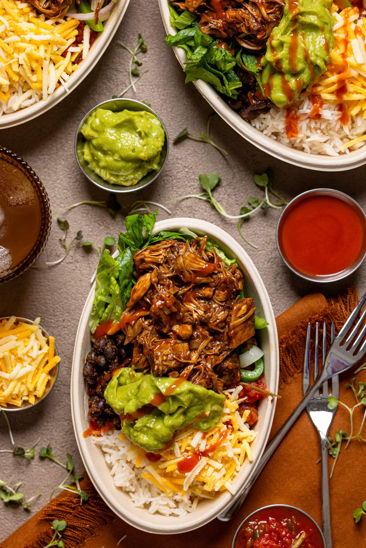 Up close shot of burrito bowls with a fork, condiments, and a drink.
