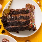 Up close shot of chocolate cake slice on a white plate with a fork with balloons.