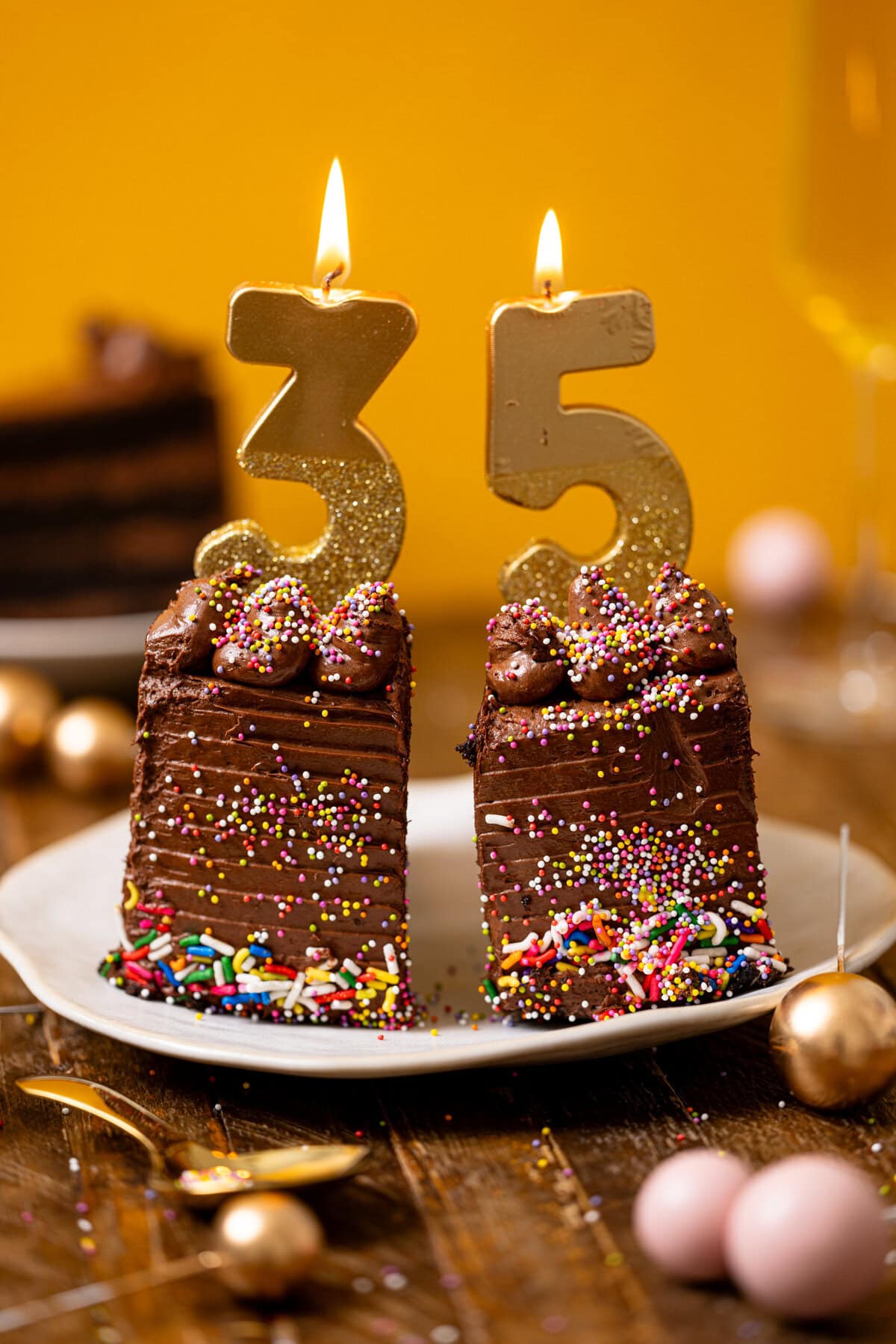 Forward shot of two cake slices with birthdays candles on a plate with a yellow background.