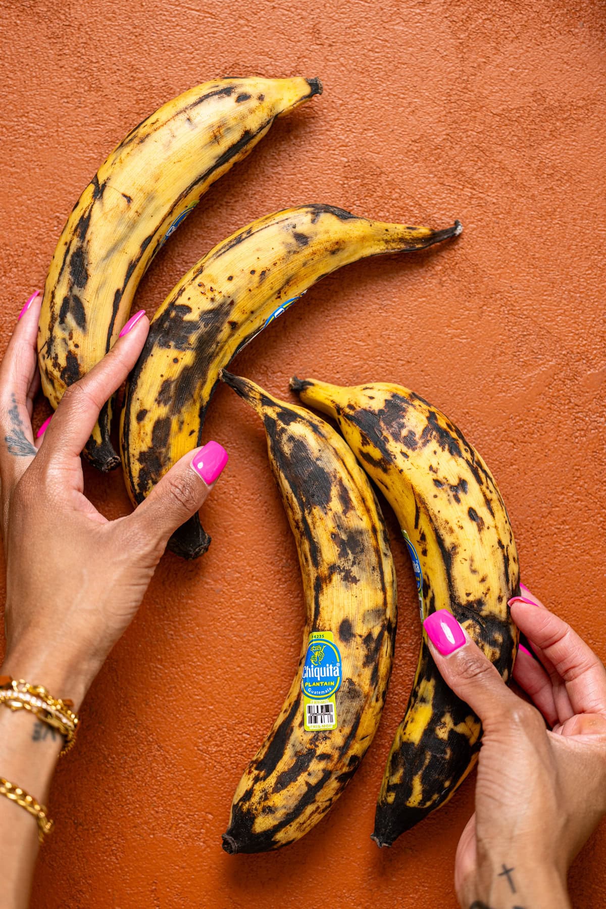 Ripe plantains being held on a burgundy table.