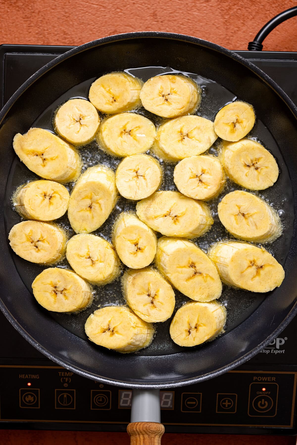 Sliced plantain in a skillet being fried.