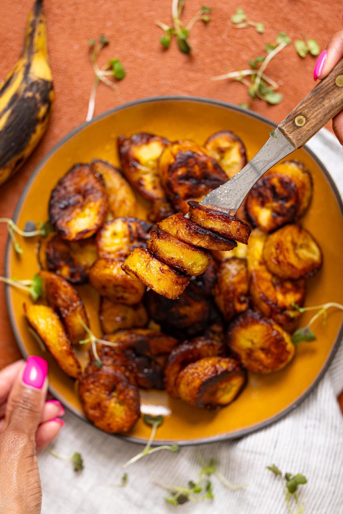 Fried sweet plantains being held with a fork and hand. 