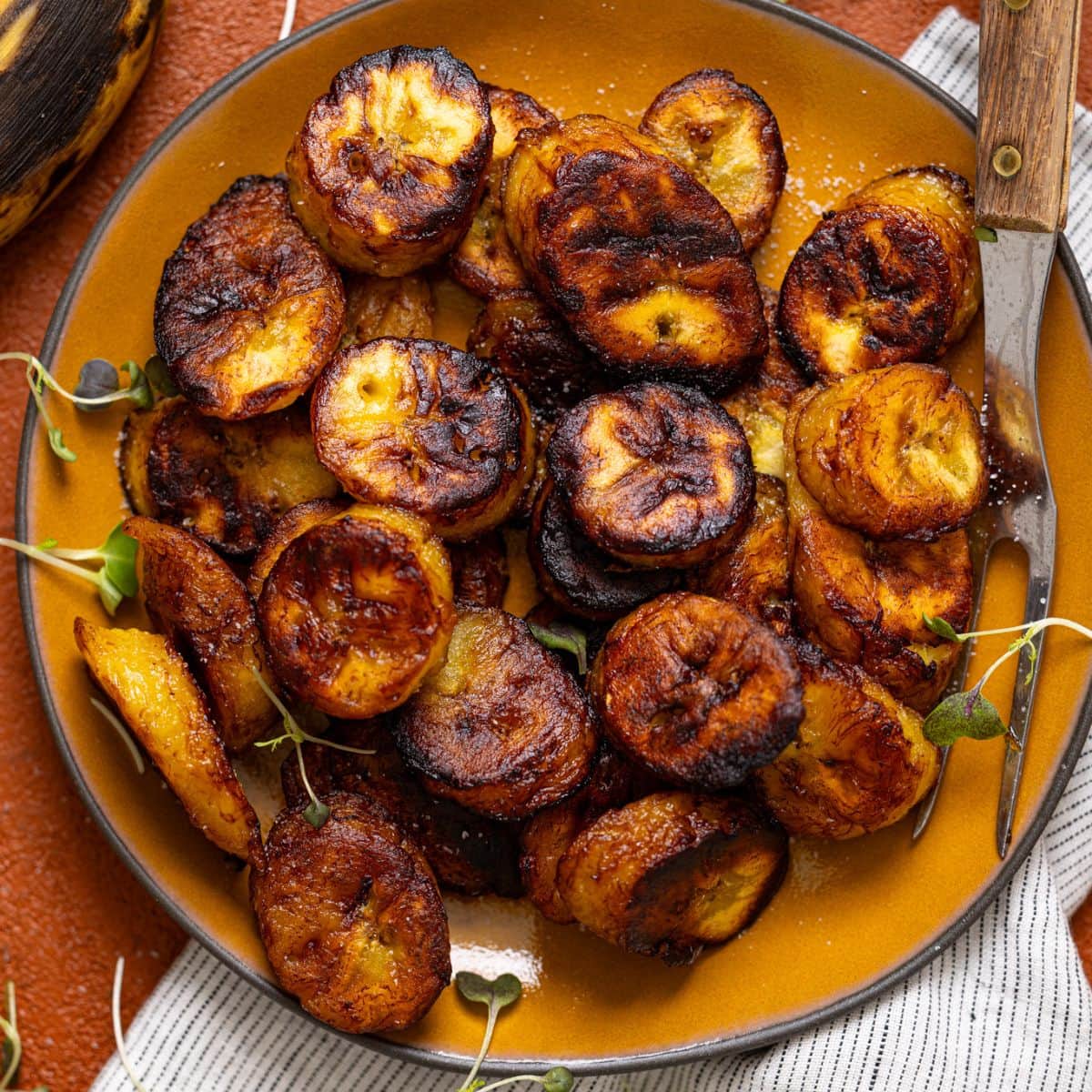 Up close shot of fried sweet plantains on a yellow plate with a fork.