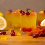 Lemon drop shots on a brown wood table with gummy bears and lemons.