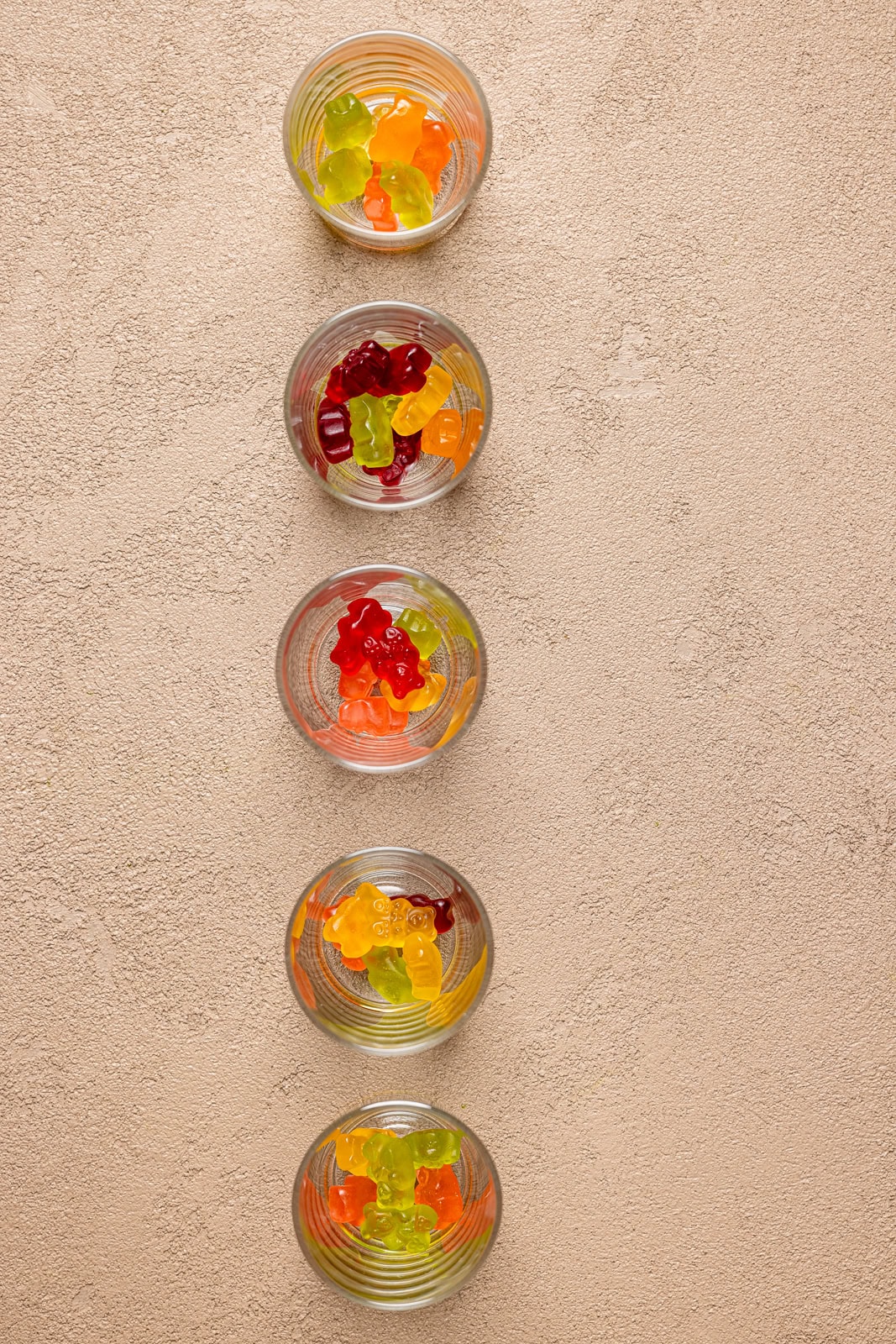 Shot glasses lined up on a table with gummy bears inside.