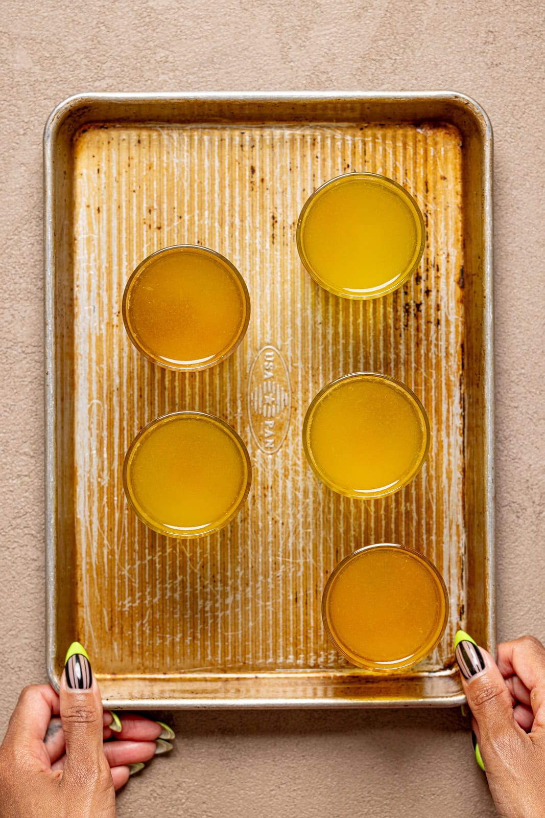 Lemon drop shots in glasses on a baking sheet being held.