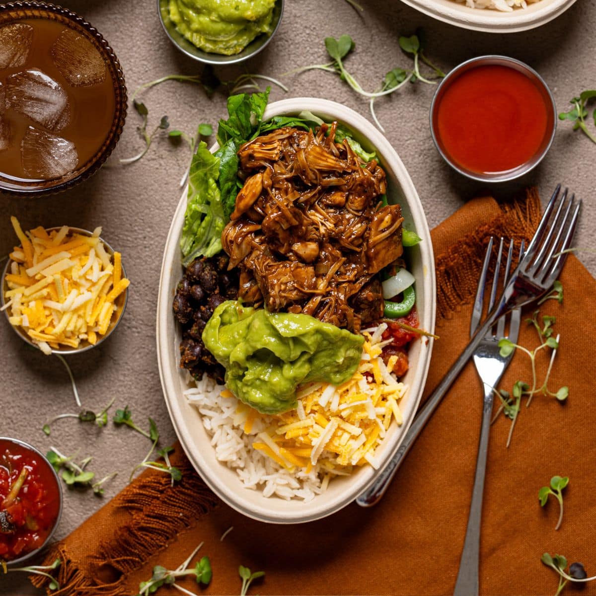 Three burrito bowls with a drink, fork, and condiments.