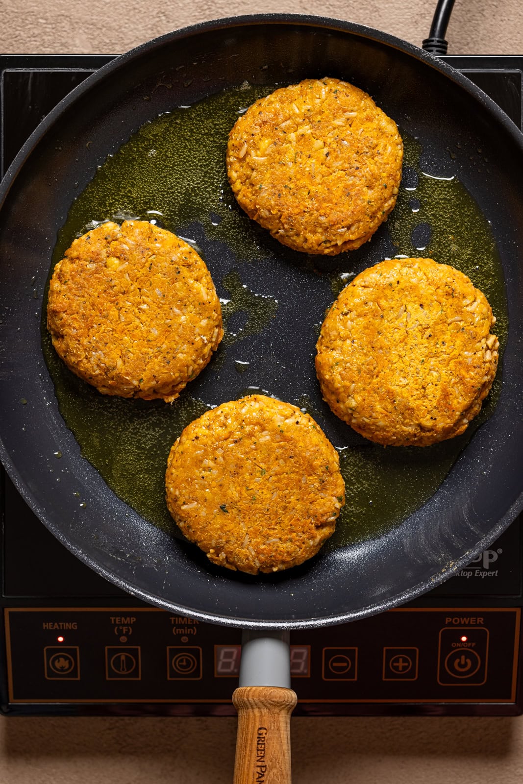 Veggie burger patties being seared in a skillet over the stovetop.